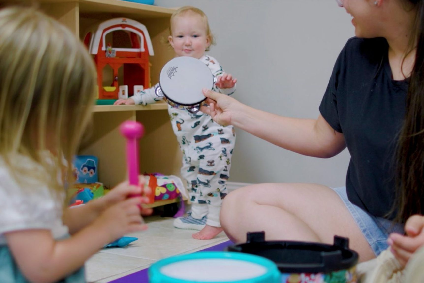 A woman hands a toy tambourine to a toddler.