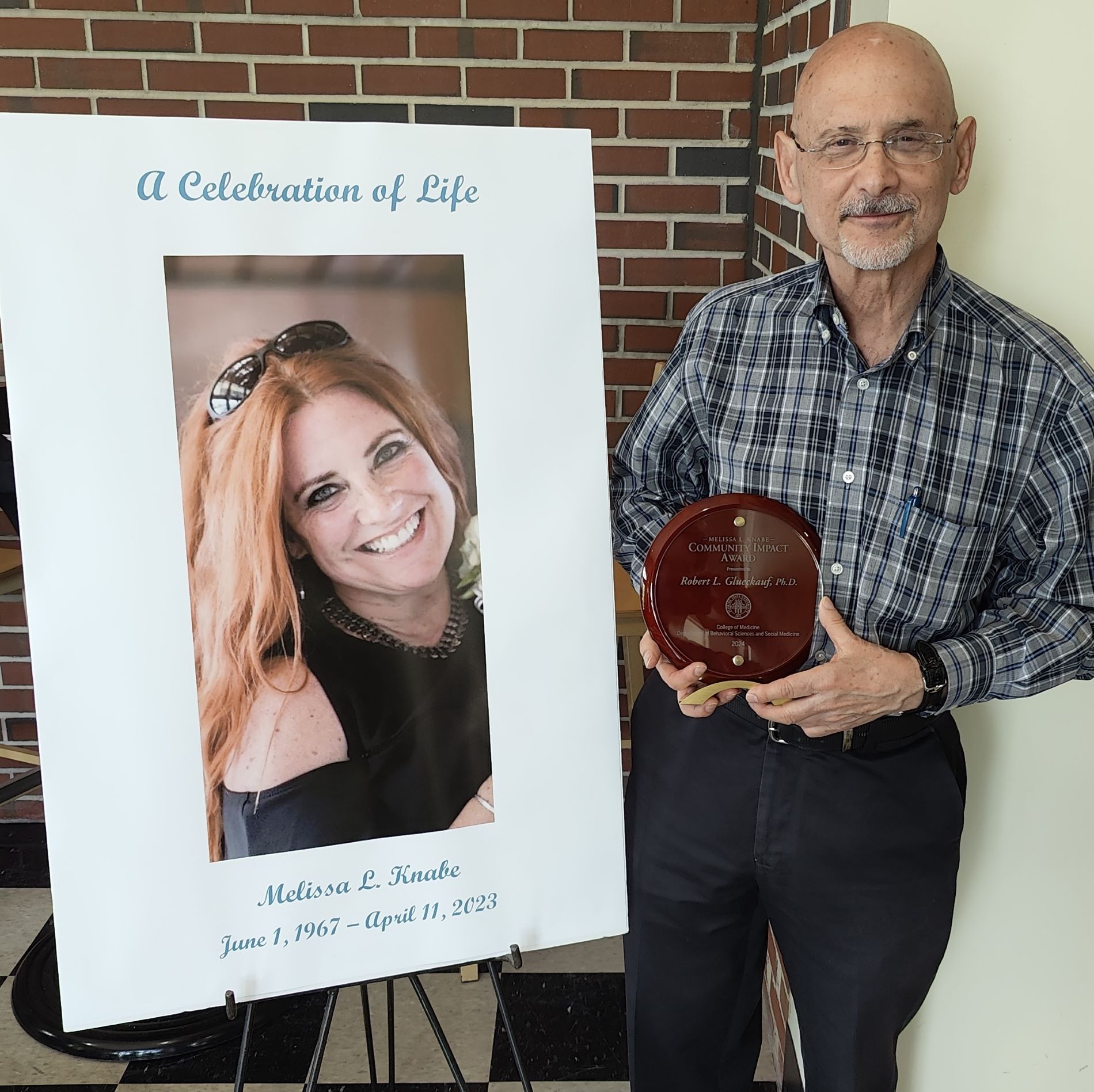 Robert Glueckauf, Ph.D. poses with his award next to a photo of the late Melissa L. Knabe.