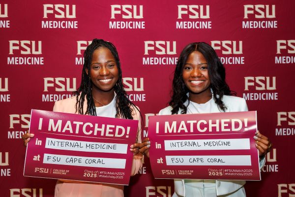 Two smiling medical students holding signs indicating their match into Internal Medicine