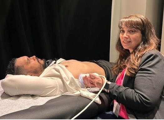 Man lying on exam table with his stomach exposed while a nurse holds probe to complete the liver scan.