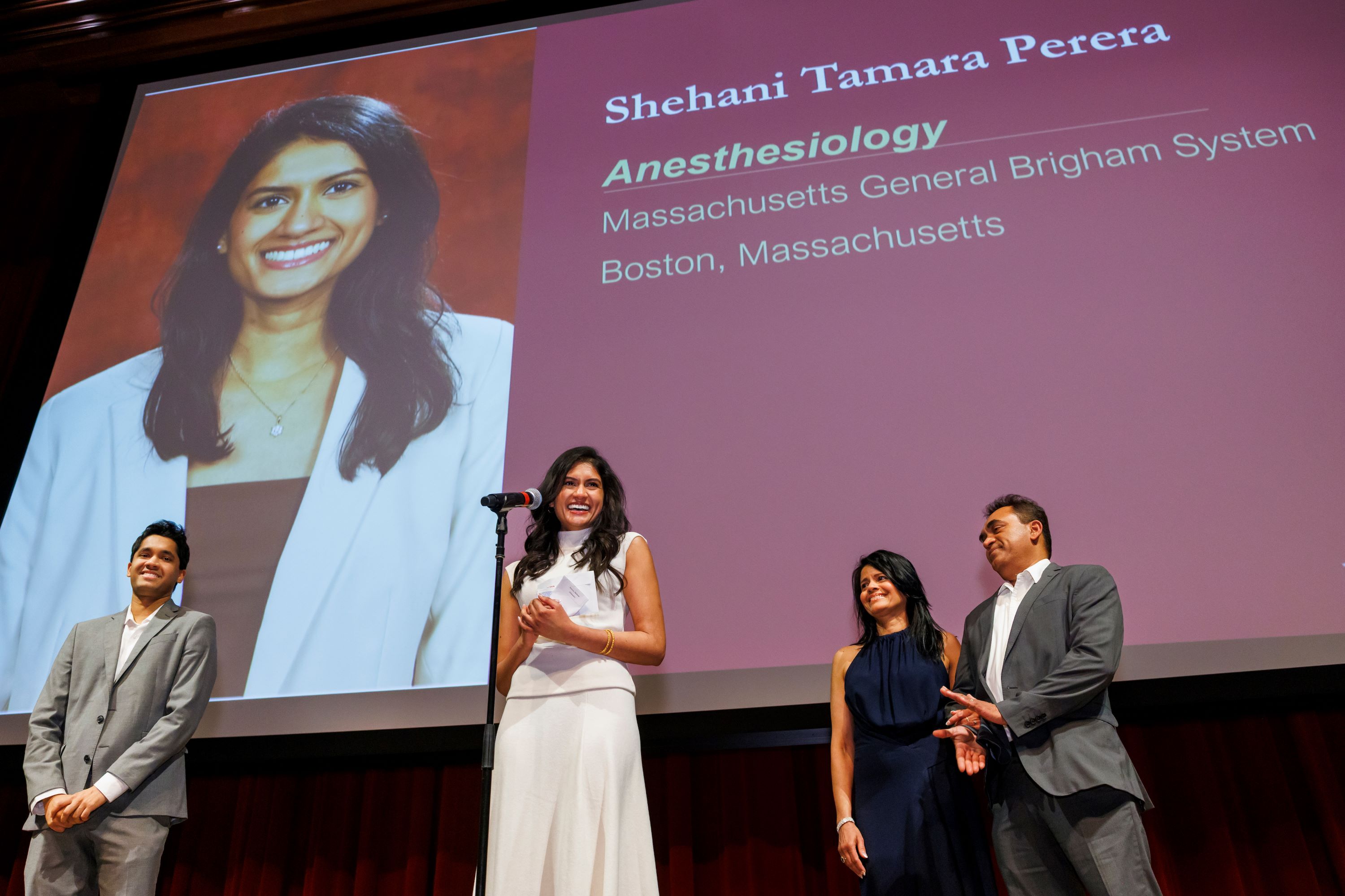 Joined on stage by her brother Ishtan, and her parents, Shea Perera announces her match. A PowerPoint slide with her photo and her match is displayed behind them.