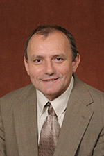 Image is a headshot of Branko Stefanovic, a white male in a tan suit in front of a burgundy background.