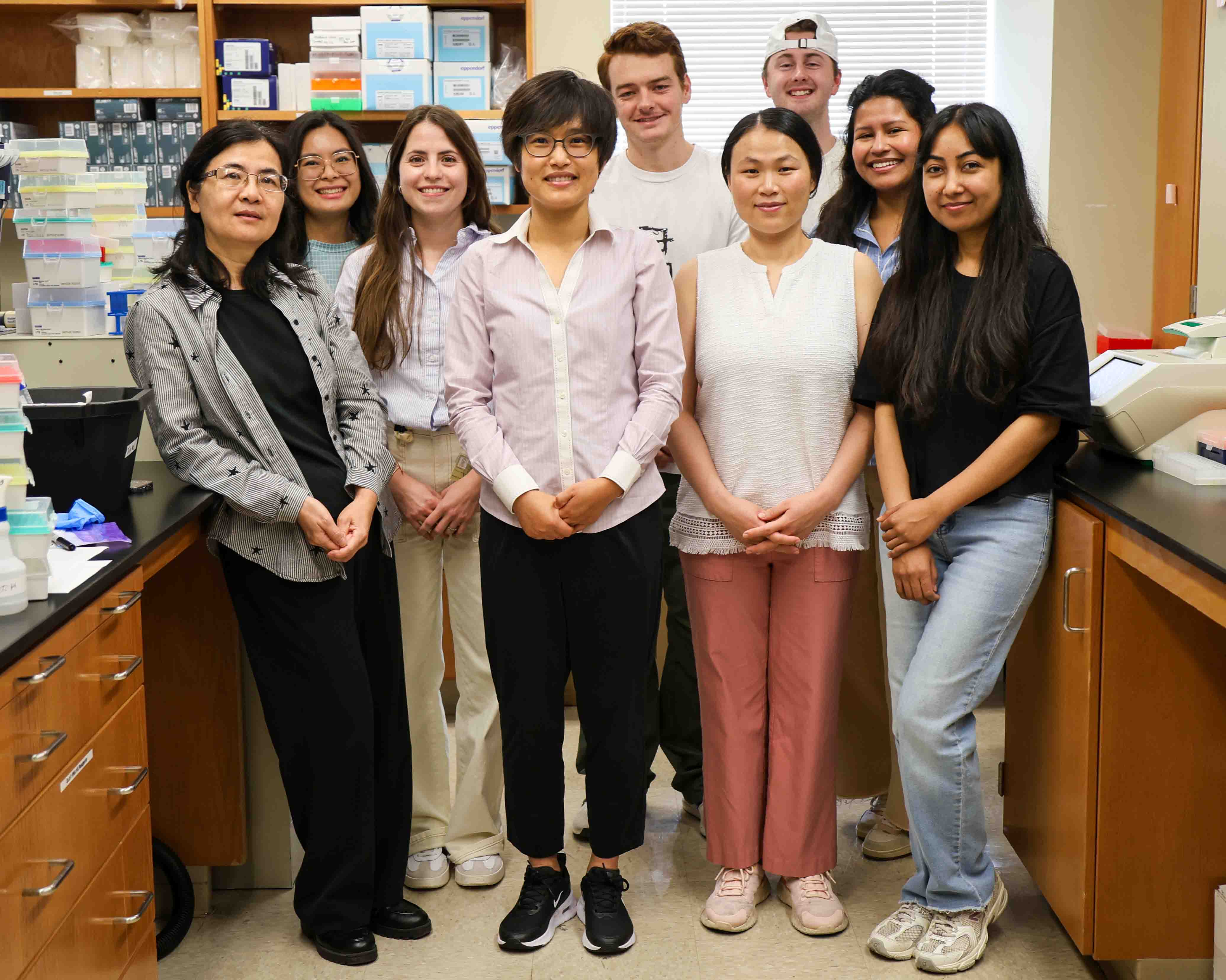 A group of eight people standing in two rows in a lab space. 