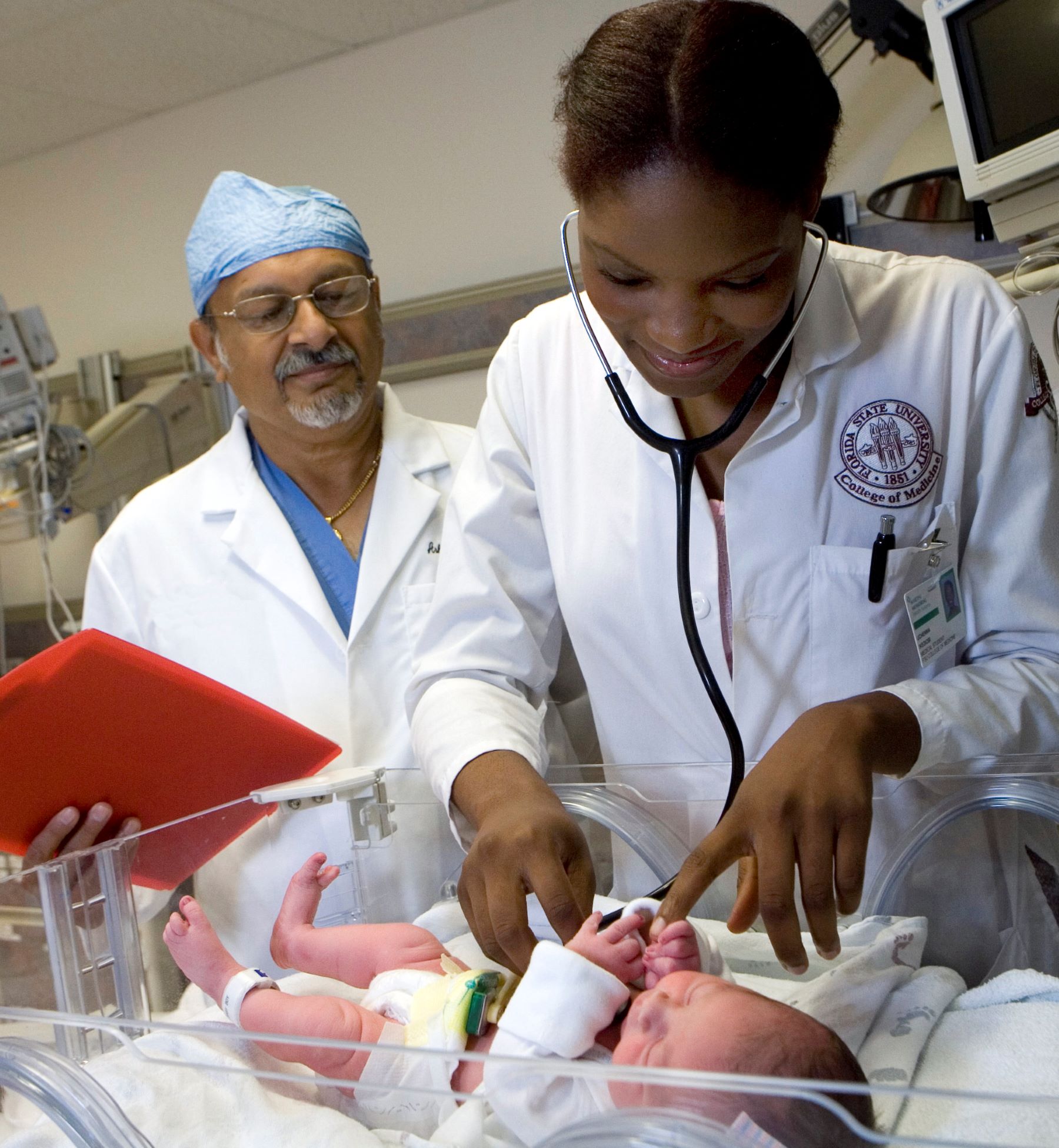 A medical student conducts a well-baby exam on an infant as the physician instructor observes.