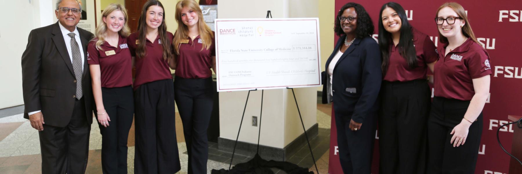 Dr. Rashmin Savani, far left; Dr. Alma Littles, M.D., to the right of the check; Darcy Sullivan, executive director of Dance Marathon at FSU and other members of the DM Executive Committee pose for a group photo after the unveiling.