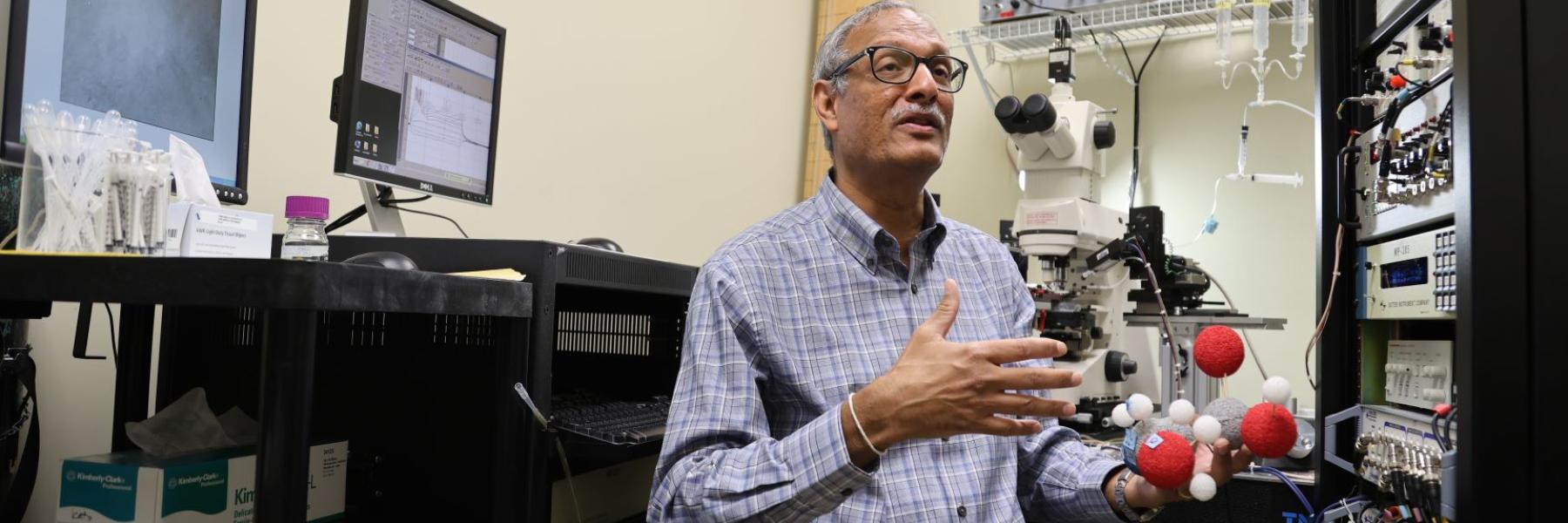 Professor Sanjay Kumar, Ph.D., holding a model of the amino acid D-serine.