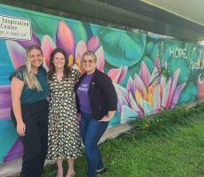 3 people standing in front of painted mural of lily pads and a dragonfly that reads “hope healing change”.