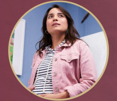 A woman with long dark hair wearing a pink denim jacket over a striped shirt, framed within a gold circular border.