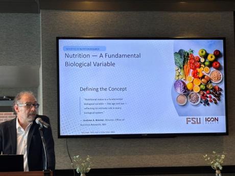Dr. Patrick Stover stands next to a slide explaining nutrition as a fundamental biological variable.