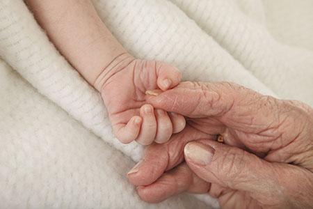 Baby and senior hold hands.