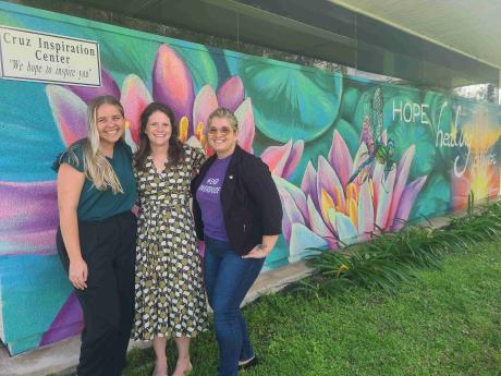 3 people standing in front of painted mural of lily pads and a dragonfly that reads “hope healing change”.
